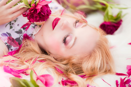 Beautiful romantic young woman in a wreath of flowers posing on a background of roses.の写真素材