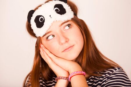 Smiling happy young redhead woman wearing striped sleeping eye maskの写真素材