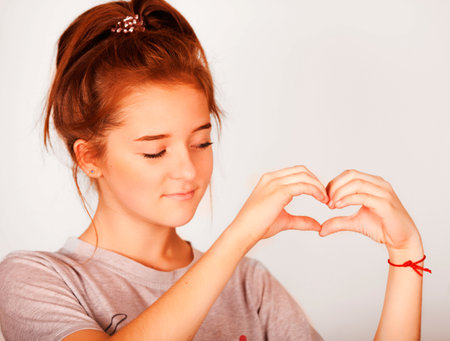 Happy beautiful girl smiling with closed eyes touching her red curly hair over white background.の写真素材