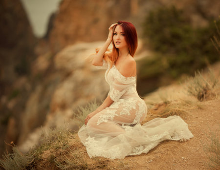 Beautiful young girl stands on a cliff of rock in an evening dressの写真素材