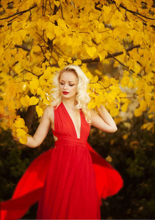 beautiful young girl with white hair in a red dress dancing in the autumn forestの写真素材