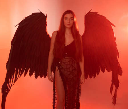 beautiful young model with big angel wings sitting in the studio. red backgroundの写真素材