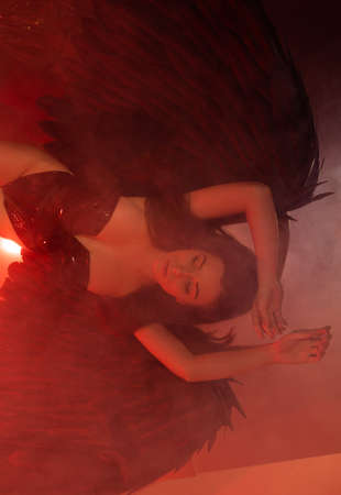 beautiful young model with big angel wings sitting in the studio. white background.black Angelの写真素材