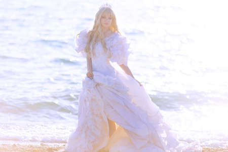 Young brunette woman in summer white dress standing on beach and looking to the sea.の写真素材