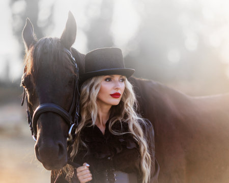 Majestic image of horse silhouette with rider on sunset background. The girl jockey on the back of a stallion rides in a hangar on a farm and jumps over the crossbarの写真素材