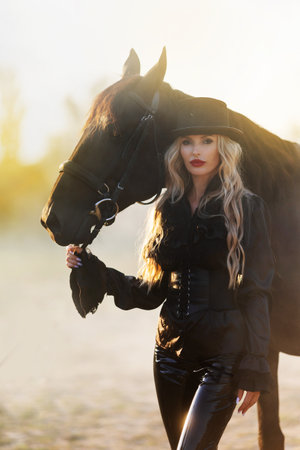 Majestic image of horse silhouette with rider on sunset background. The girl jockey on the back of a stallion rides in a hangar on a farm and jumps over the crossbarの写真素材
