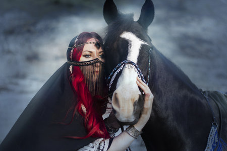 Portrait of a beautiful girl with red hair and a black horseの写真素材