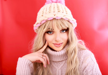Portrait of a beautiful blonde woman in winter clothes on a red background.