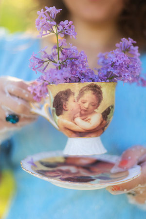 A girl in a blue dress holds a cup with lilac flowersの写真素材