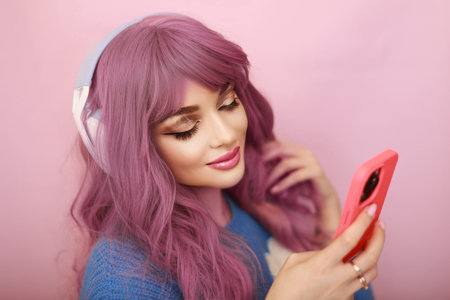 beautiful young woman with pink hair and headphones listening to music on smartphoneの写真素材