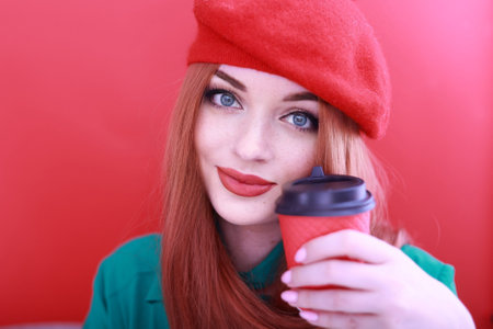 Romantic young woman holding a paper red cup with coffee or tea. red-haired girl in a bright red headdress.の写真素材