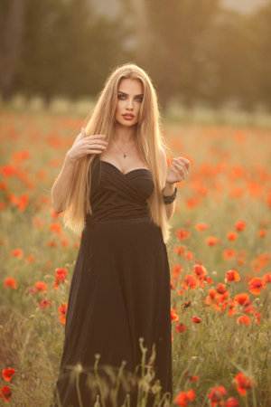 a girl in a black dress on a poppy field at sunset.の写真素材