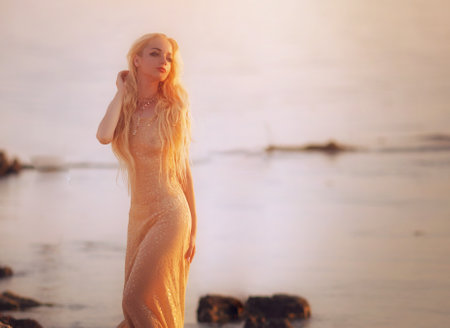 Beautiful blonde girl in a long dress on the beach at sunsetの写真素材