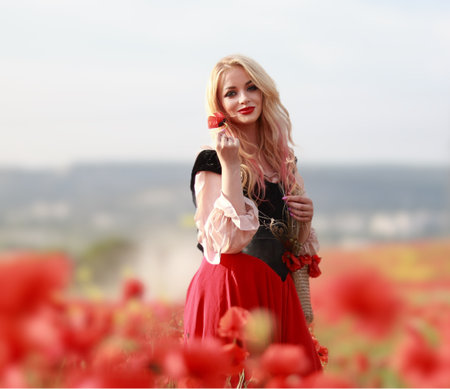 A girl in a vintage dress walks among red poppy flowers at sunset.の写真素材
