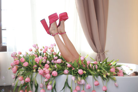 a bathroom full of pink tulips. Feet in pink glamorous shoes are visible from the bathroomの写真素材