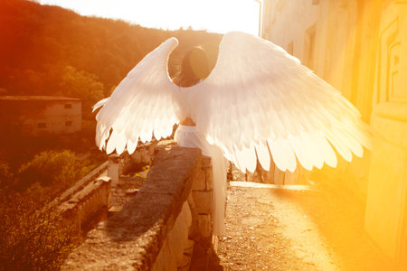 an angel girl with big white wings stands on a mountain at dawn. Early morning, angel on the...