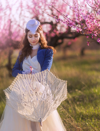 Vintage. Beautiful young woman in retro clothes, hat in a blooming garden. Visual for content.の写真素材