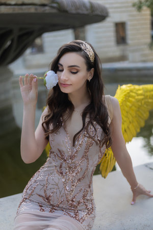 Artistic photo A fantasy female angel with golden wings looks at the background of architecture. Fairy girl sexy lady fashion model poseの写真素材