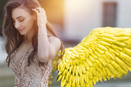 Artistic photo A fantasy female angel with golden wings looks at the background of architecture. Fairy girl sexy lady fashion model poseの写真素材