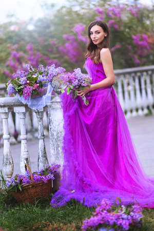 Fashion Model in Lilac Flowers, Young Woman in Beautiful Long Dress Waving on Wind, Outdoor Beauty Portrait in Blooming Gardenの写真素材