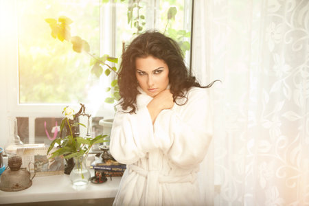 a cute smiling girl in a white robe rests on a bed early in the morning, next to a plate of oatmeal porridgeの写真素材