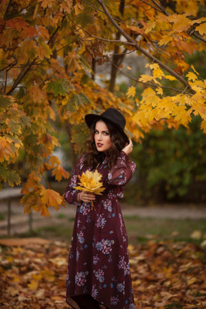 Hello autumn. Seen from behind middle aged woman in red hat with scarf and gloves rejoicing in the city park.の写真素材