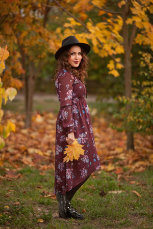 Hello autumn. Seen from behind middle aged woman in red hat with scarf and gloves rejoicing in the city park.の写真素材