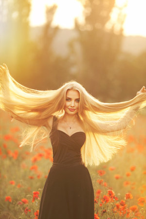 a girl in a black dress on a poppy field at sunset. warm summer eveningの写真素材
