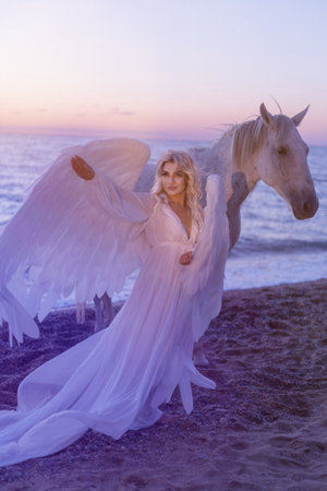 Young long hair woman in white dress posing with white horse on seascape backgroundの写真素材