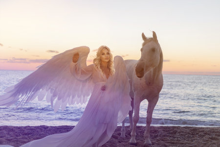 Young long hair woman in white shirt with white horse on seascape backgroundの写真素材