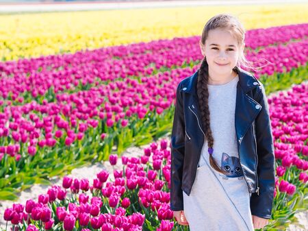 Cute teenager girl with long hair smelling tulip flower on tulip fields in Amsterdam region, Holland, Netherlands. Magical Netherlands landscape with tulip field in Holland Trevel and spring concept.の写真素材