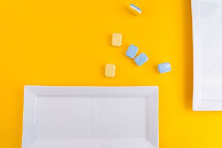 Cleaning dishwasher tablets with white plate on a yellow background. Group of bright colored soap...