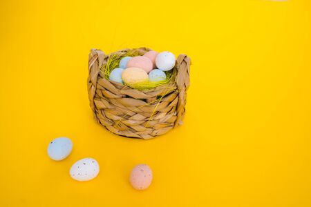 Easter holiday decorations on yellow background. Colorful easter painted speckled eggs in basket. Creative spring composition with Easter elements - flowers and eggs. Traditional Easter Celebrating.の写真素材