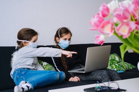 Online education, distance learning, home schooler. Childeren in medical mask studying homework during online lesson at home in digital tablet of laptop. Social distance on quarantine. Self-isolationの写真素材