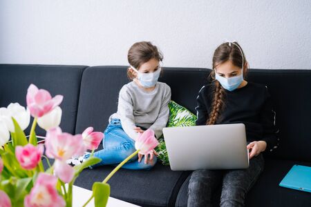 Online education, distance learning, home schooler. Childeren in medical mask studying homework during online lesson at home in digital tablet of laptop. Social distance on quarantine. Self-isolationの写真素材