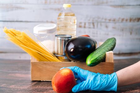 Food supplies. Crisis food box stock for coronavirus quarantine isolation period in wood background. Different food in aluminum cans, Rice, pasta, oil, fruit, vegetable. Food delivery, Donation.の写真素材