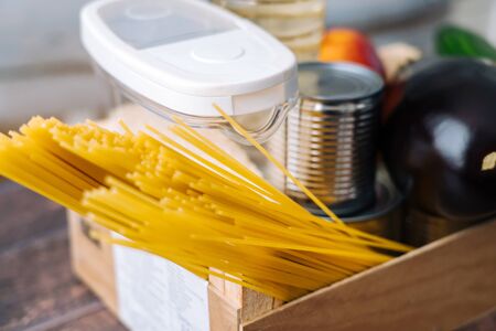 Food supplies. Crisis food box stock for coronavirus quarantine isolation period in wood background. Different food in aluminum cans, Rice, pasta, oil, fruit, vegetable. Food delivery, Donation.の写真素材