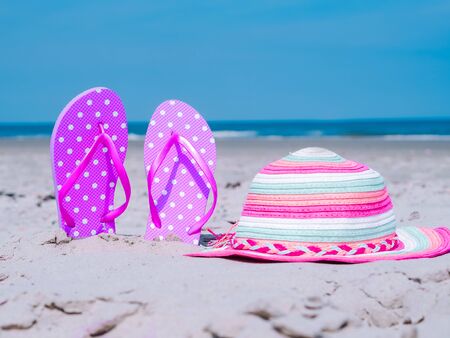 Summer composition with beach cccessories beach flip flops and colorful hat on tropical sand against blue sea and sky background. summer vacation concept of beach holiday, sea tour, warm sunny summer.の写真素材