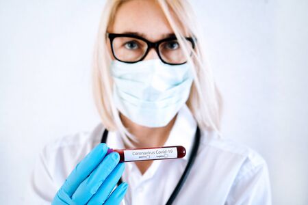 Coronavirus Covid-19 outbreaking. Doctor in medical glove and face mask holding tube with blood test result for rapidly spreading Coronavirus 2019-nCoV in laboratory. Medicine and epidemic concept.の写真素材