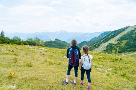 Children hiking on beautiful summer day in alps mountains Austria, resting on rock and admire amazing view to mountain peaks. Active family vacation leisure with kids.Outdoor fun and healthy activity.の写真素材