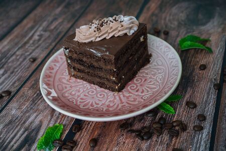 Piece of Chocolate cake with cream on plate. Chocolate cake on wooden background with coffee beans...