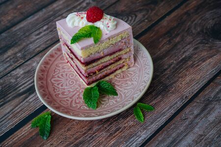 Tasty piece of raspberry multi-layered cake on plate. raspberry cake served for dessert on wooden background with mint leaves. Delicious slice tart on plate. Baking and decorating raspberry cakeの写真素材