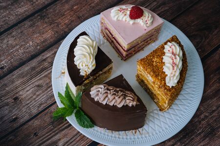 Collection of various cakes on wood background. Assortment of pieces slices with cream. Plate with...