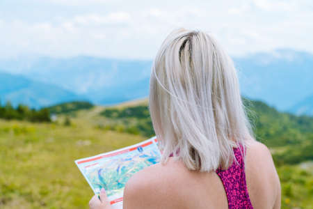 Woman hiking on beautiful summer day in alps mountains Austria resting on rock. Girl standing back and look at map mountain peaks in valley. Active family vacation. Outdoor fun and healthy activity.の写真素材