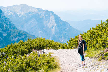 Children hiking on beautiful summer day in alps mountains Austria, resting on rock and admire amazing view to mountain peaks. Active family vacation leisure with kids. Outdoor fun and healthy activityの写真素材