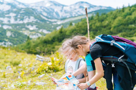 Children hiking on beautiful summer day in alps mountains Austria resting on rock. Kids look at map mountain peaks in valley. Active family vacation leisure with kids.Outdoor fun and healthy activityの写真素材