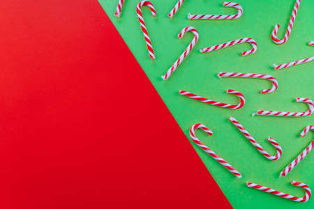Holiday minimalist decorations. Christmas composition. Present box, Xmas candy canes, red festive decorations on red and green background. Copy space. Xmas and new year holiday concept.の写真素材