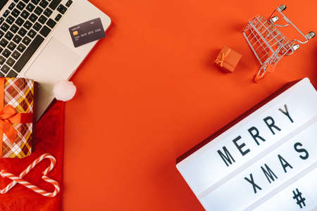 Christmas online shopping on laptop with credit card. New year decorations candy canes, shopping cart and presents box top view flat lay on red background. Merry Xmas winter holidays sales concept.の写真素材