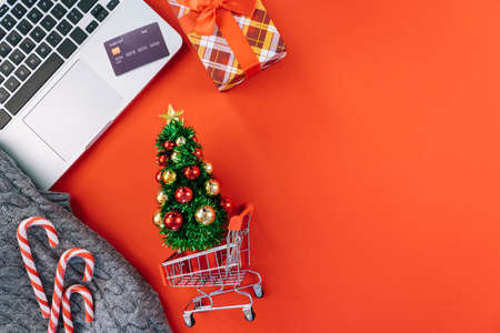 Christmas online shopping on laptop with credit card. New year decorations candy canes, shopping cart and presents box top view flat lay on red background. Merry Xmas winter holidays sales concept.の写真素材