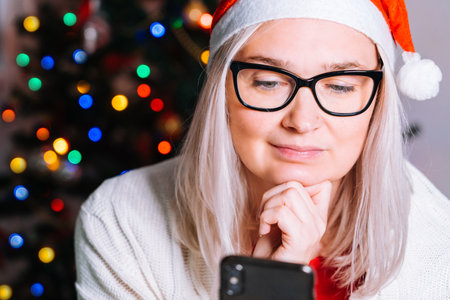 Christmas online family congratulations. Smiling girl at home using laptop computer notebook for video call friends and parents in Santa hat. Woman looking camera and waving greeting handsの写真素材